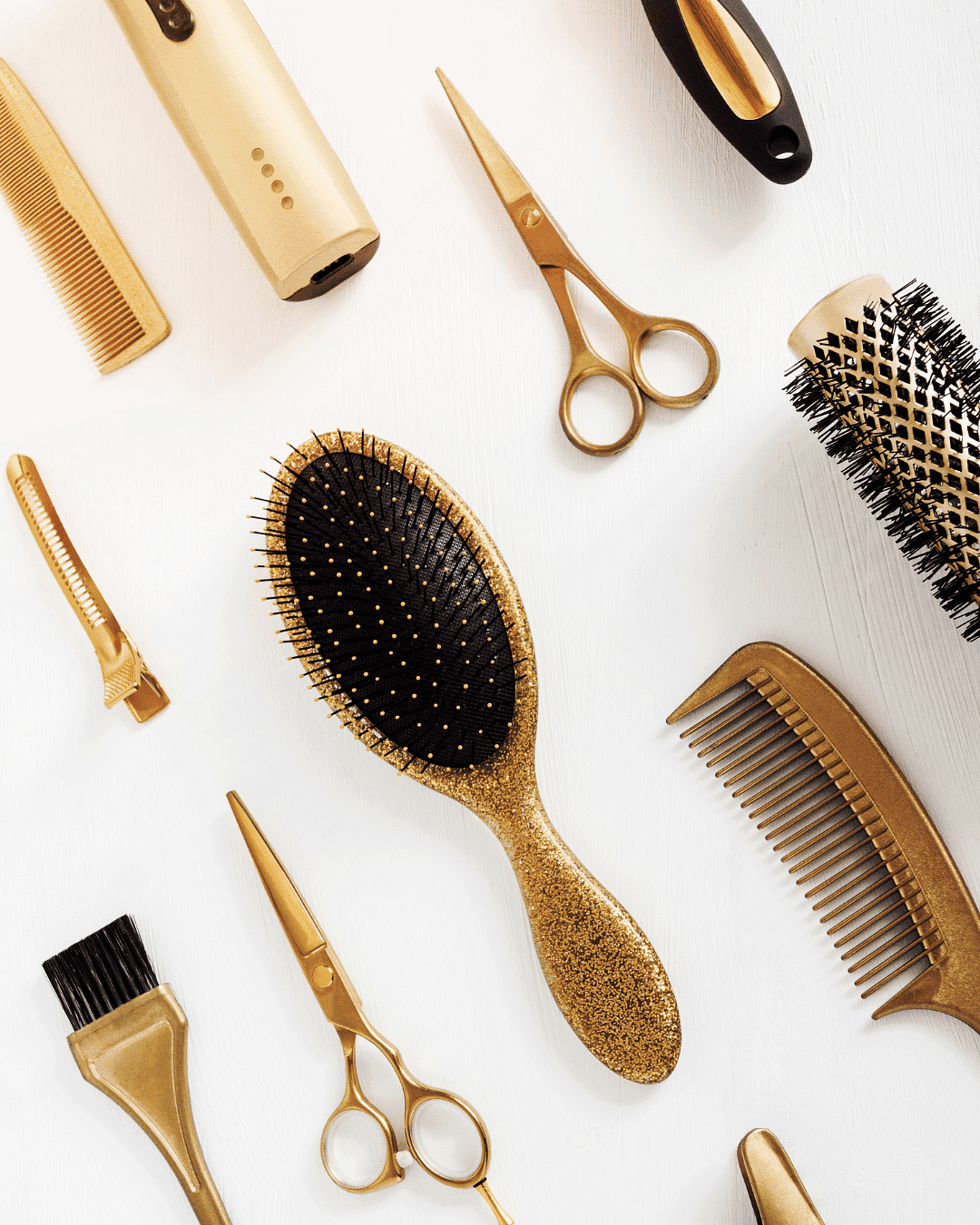 Gold and black hair styling tools, including brushes, combs, and scissors, arranged on white.