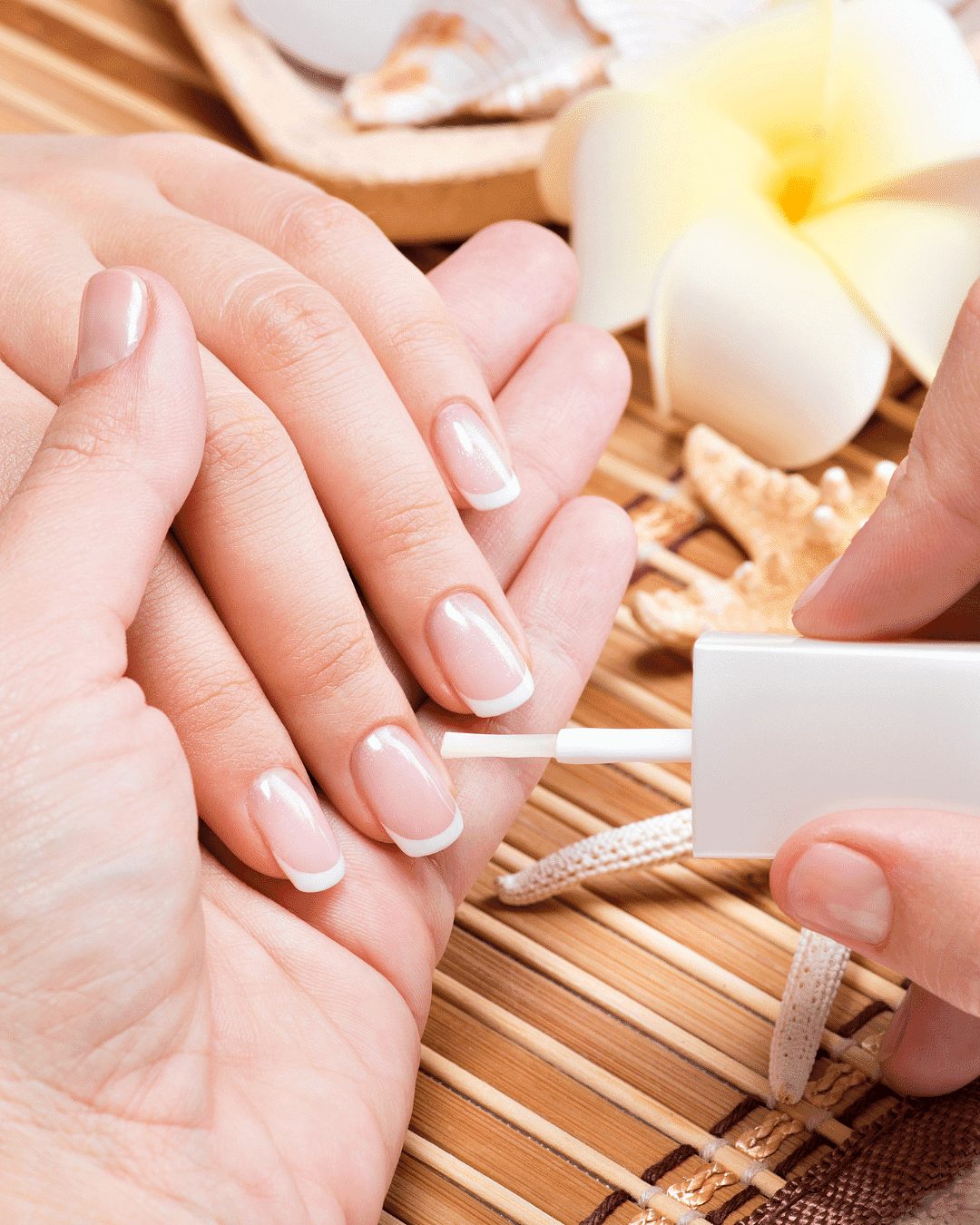 Person getting a French manicure with white nail polish on a bamboo mat, tropical decor around.